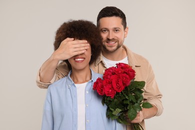 International dating. Handsome man presenting roses to his beloved woman on light grey background