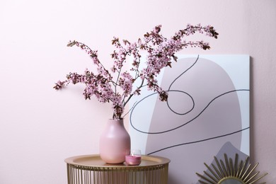 Photo of Blossoming tree twigs in vase on table near pink wall indoors