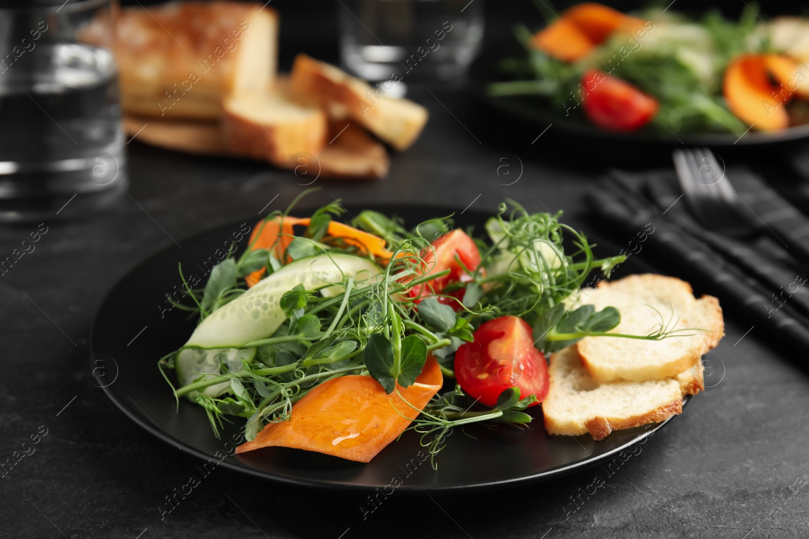 Photo of Delicious vegetable salad with microgreen served on black table