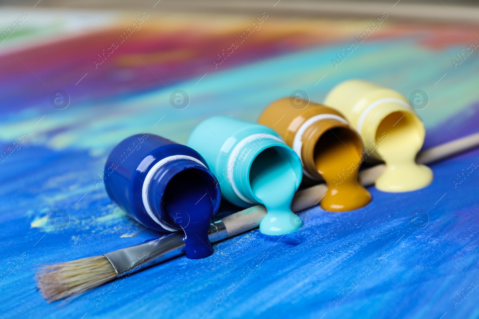 Photo of Jars with paints and brush on abstract picture, closeup