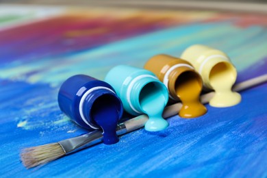 Photo of Jars with paints and brush on abstract picture, closeup