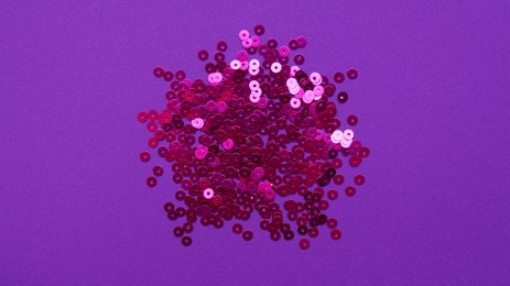 Pile of bright sequins on purple background, top view