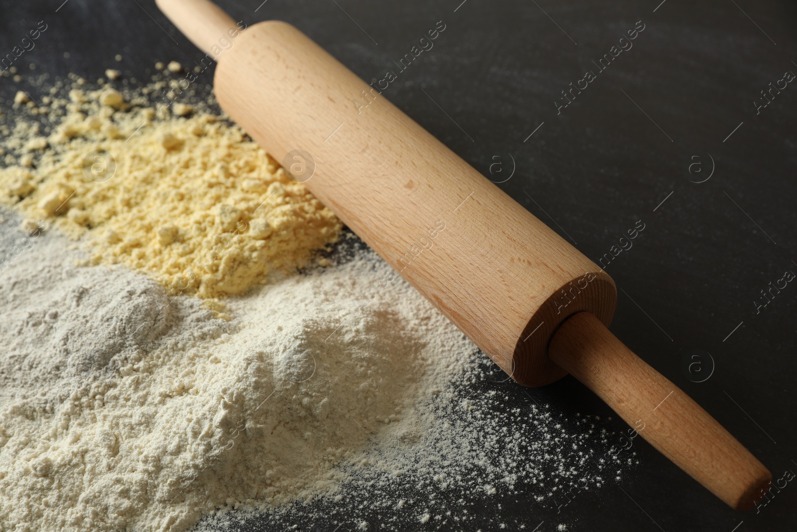 Photo of Rolling pin and different types of flour on black table, closeup