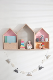 Photo of Cute house shaped shelves and garland on white wall. Children's room interior design