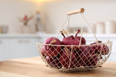 Photo of Basket with red onions on wooden table in kitchen