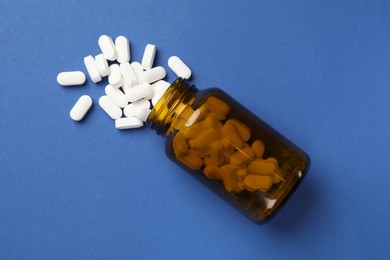 Photo of Vitamin pills and bottle on blue background, top view