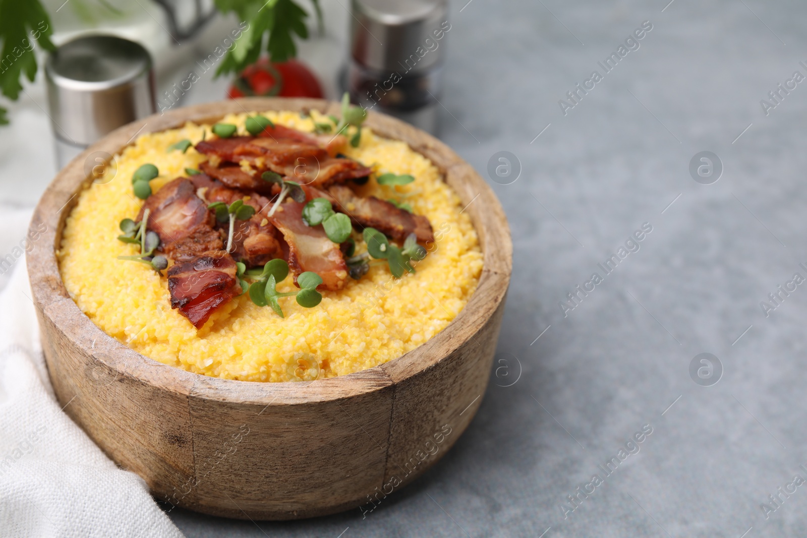 Photo of Cooked cornmeal with bacon and microgreens in bowl on light grey table, closeup. Space for text