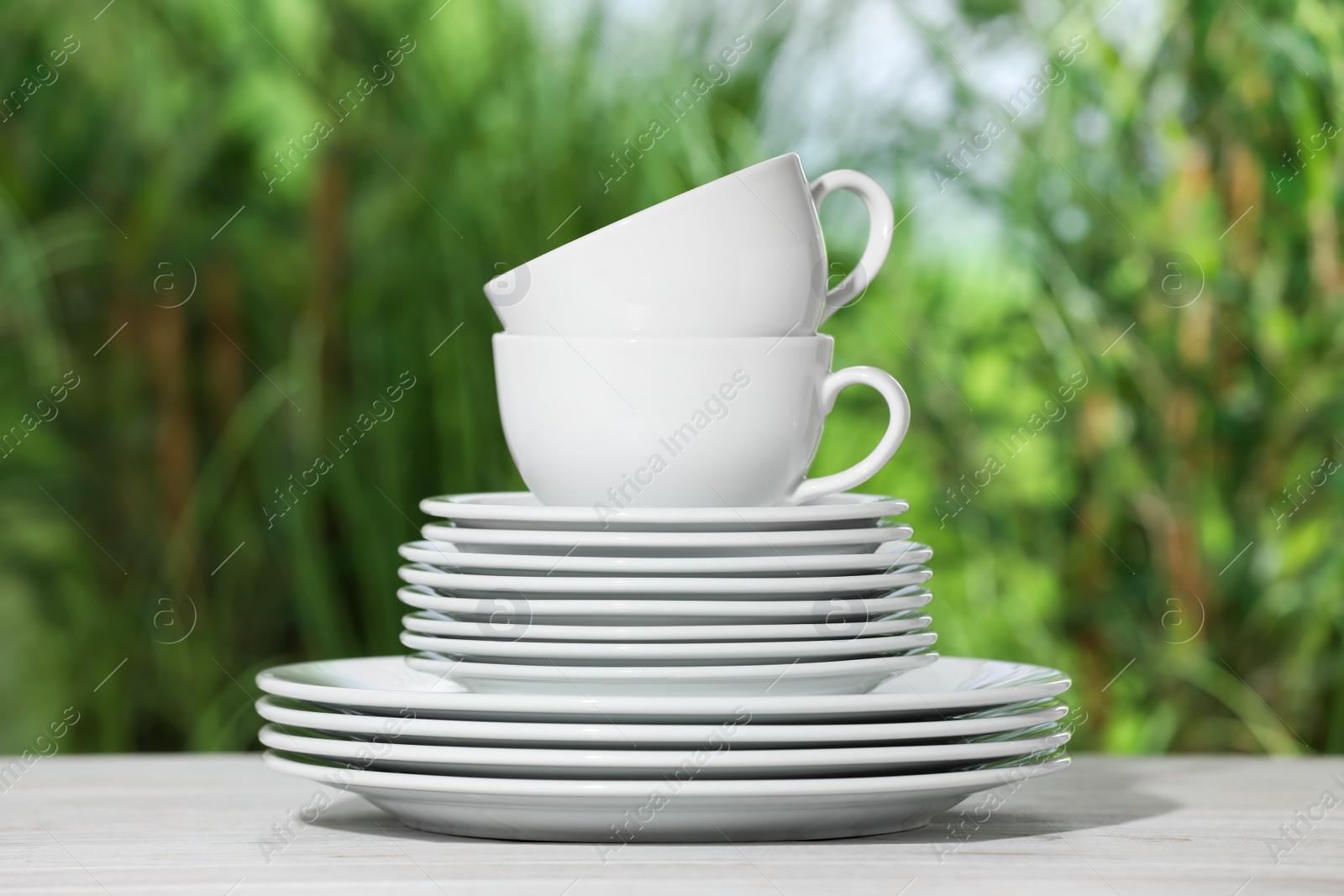 Photo of Set of clean plates and cups on white table against blurred background