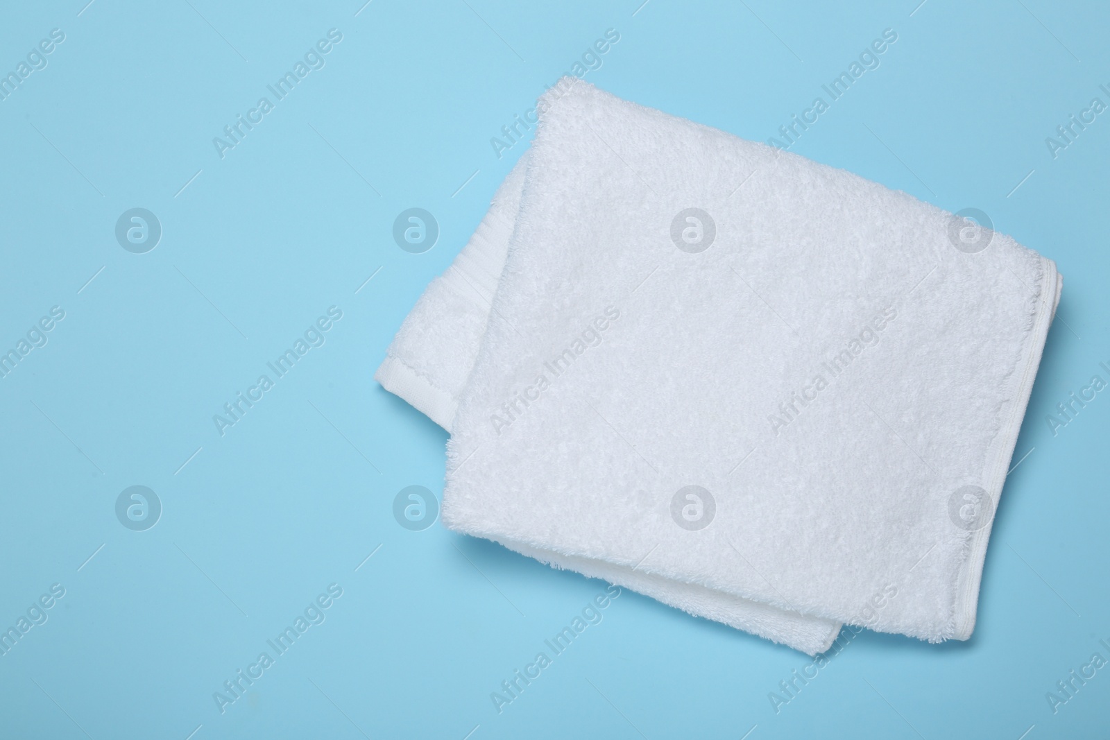 Photo of White terry towel on light blue background, top view. Space for text