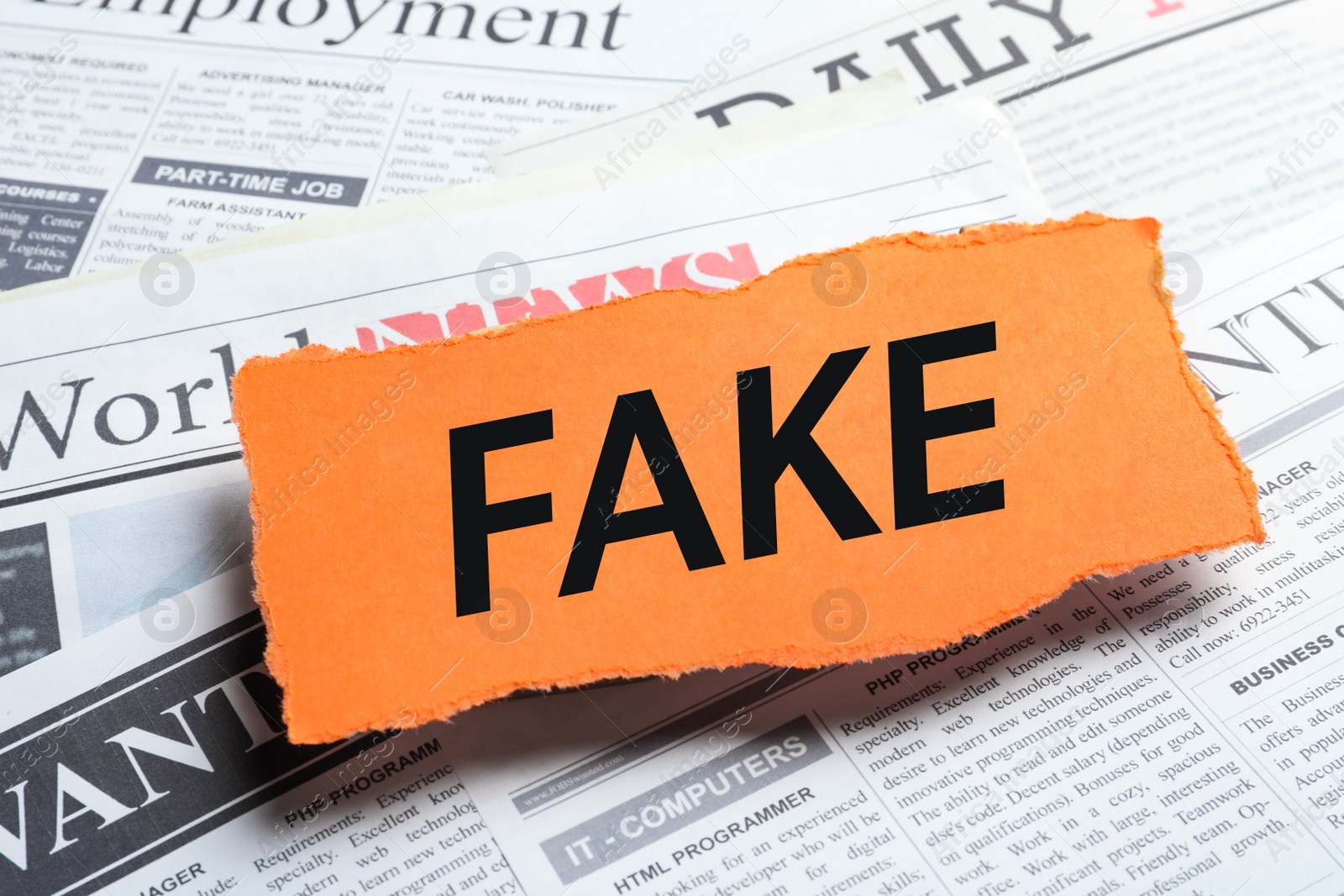 Photo of Orange paper piece with word FAKE on pile of newspapers, closeup