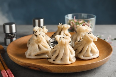 Photo of Wooden plate with tasty baozi dumplings and sesame seeds on table