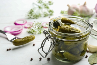 Glass jar of pickled cucumbers on white wooden table. Space for text