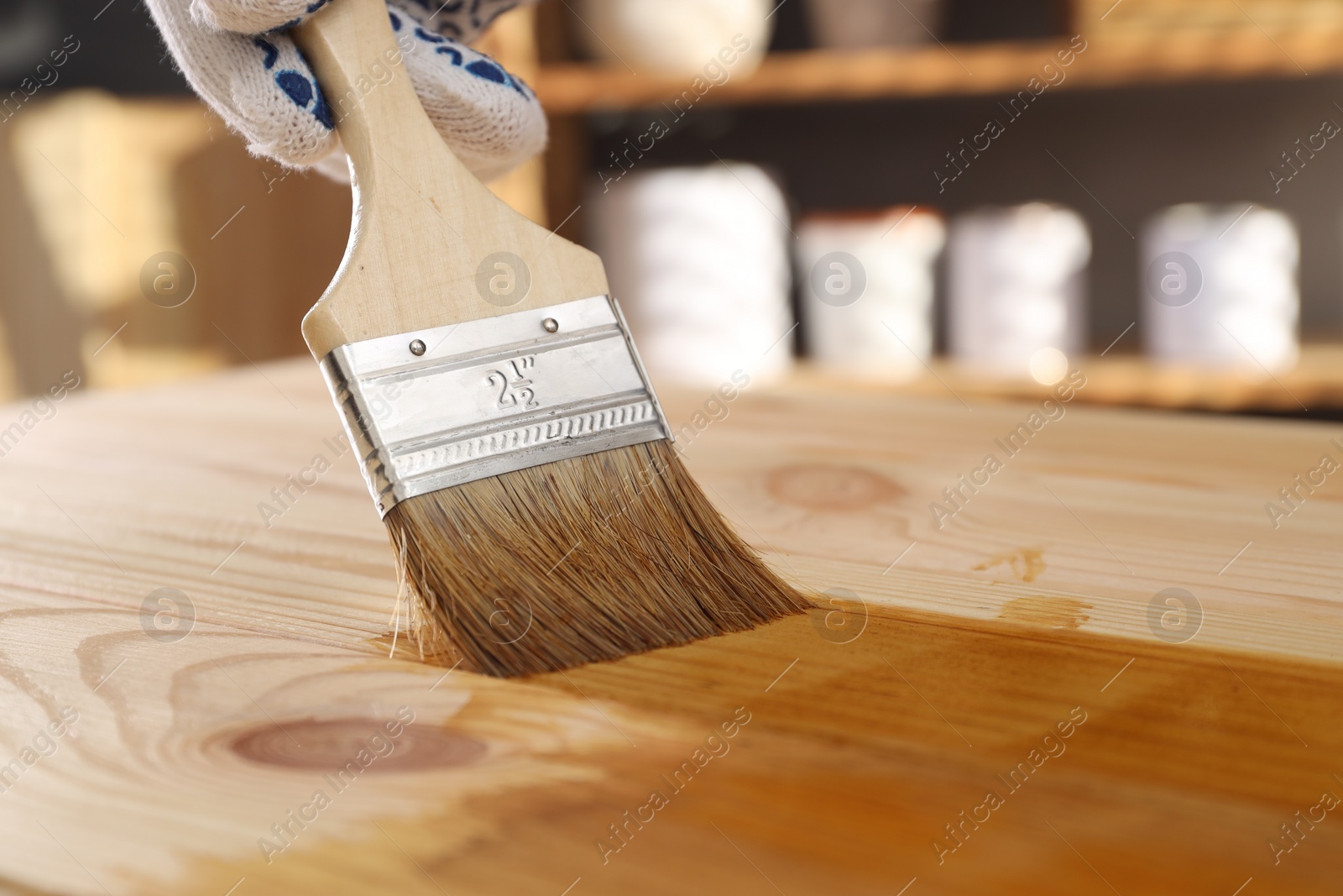 Photo of Man with brush applying wood stain onto wooden surface indoors, closeup