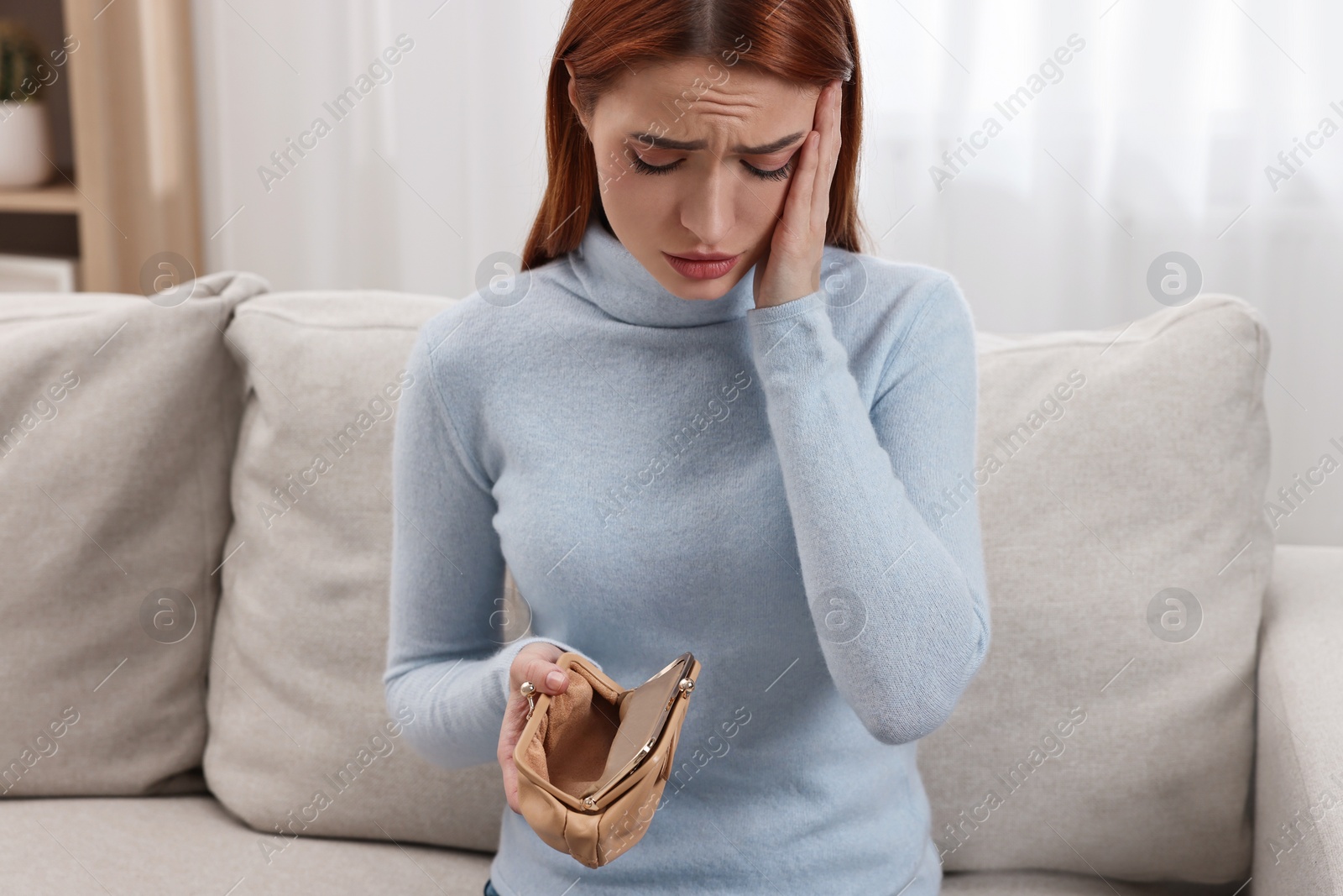 Photo of Upset woman with empty wallet on sofa indoors