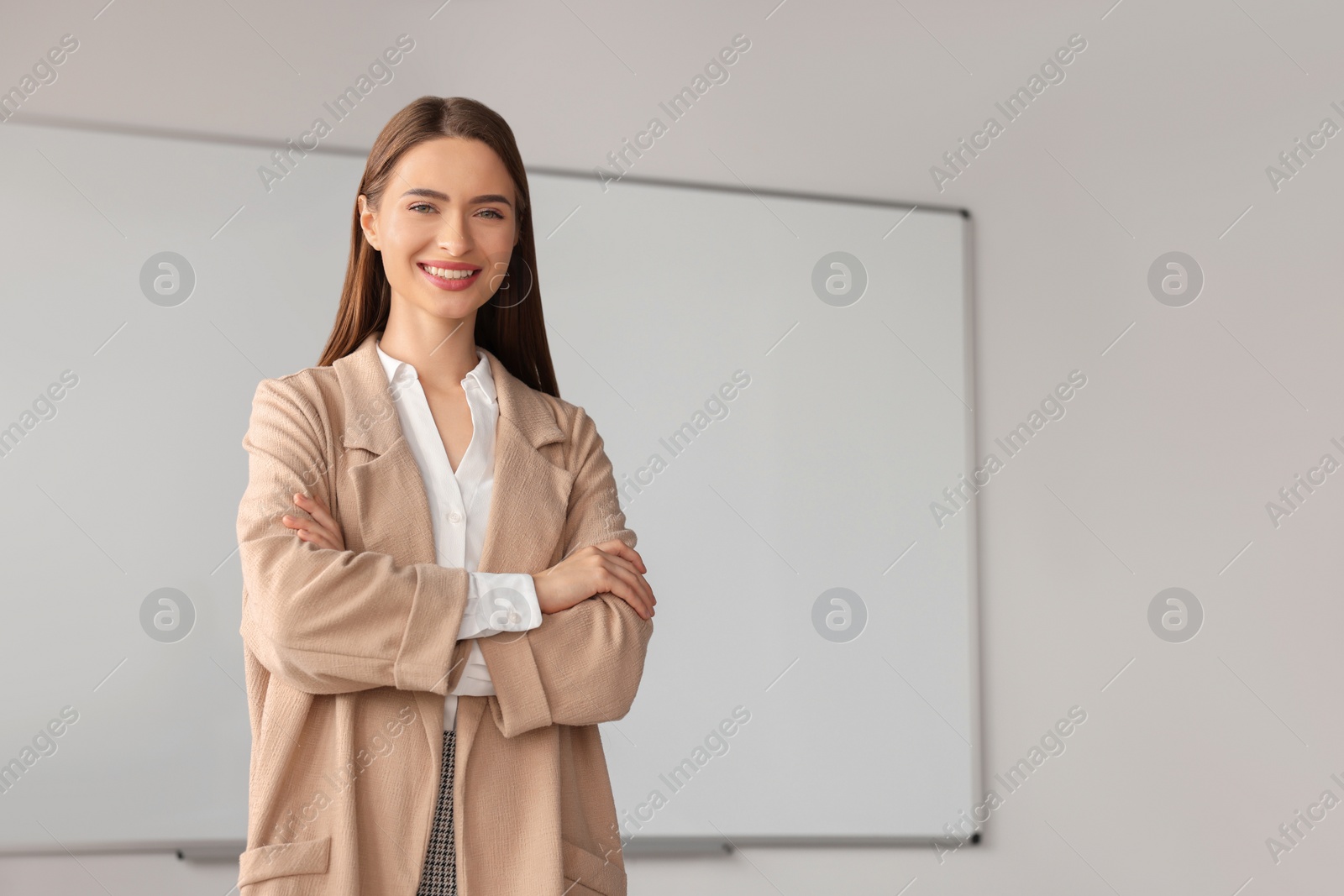 Photo of Happy young teacher at whiteboard in classroom. Space for text