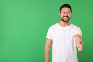 Photo of Happy man welcoming and offering handshake on green background. Space for text