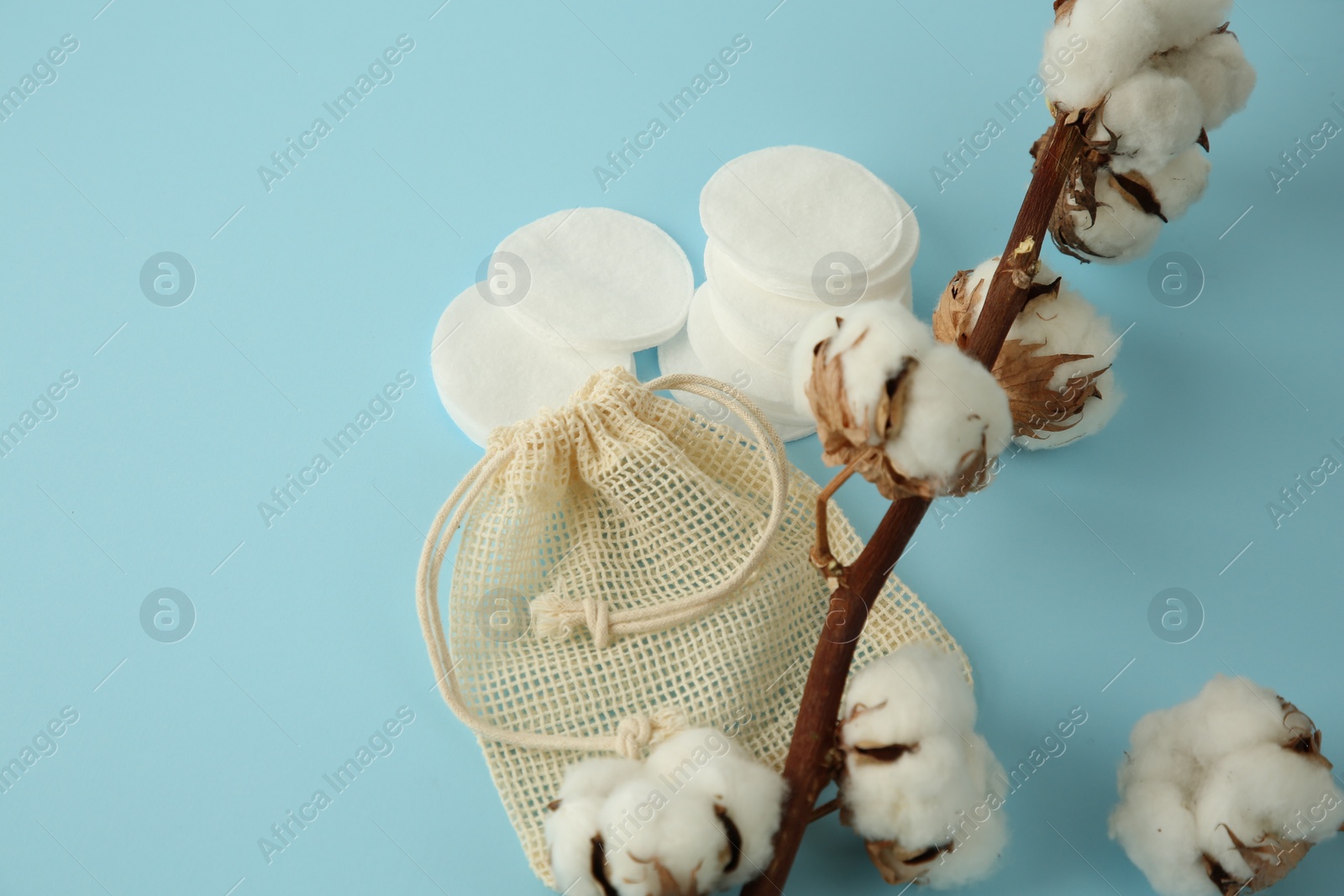 Photo of Bag, cotton pads and flowers on light blue background