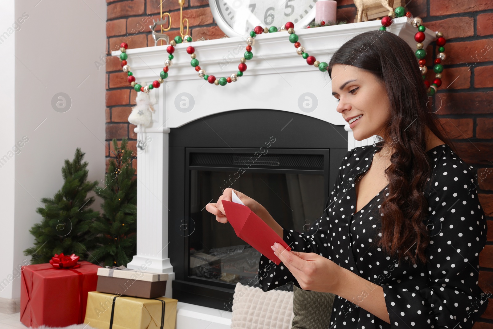 Photo of Young woman with greeting card sitting near fireplace indoors