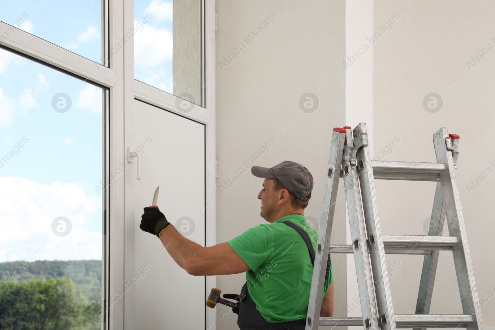 Photo of Worker holding knife and hammer indoors. Window installation