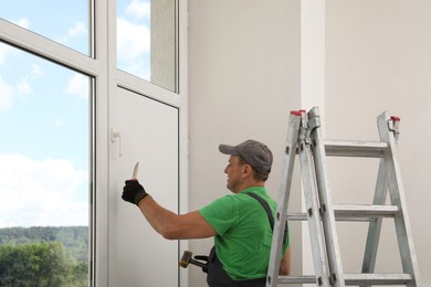 Worker holding knife and hammer indoors. Window installation