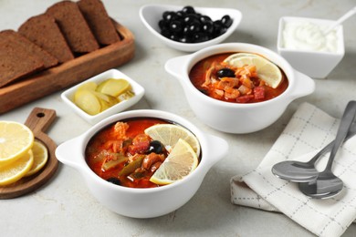 Meat solyanka soup with sausages, olives, vegetables and spoons on white textured table