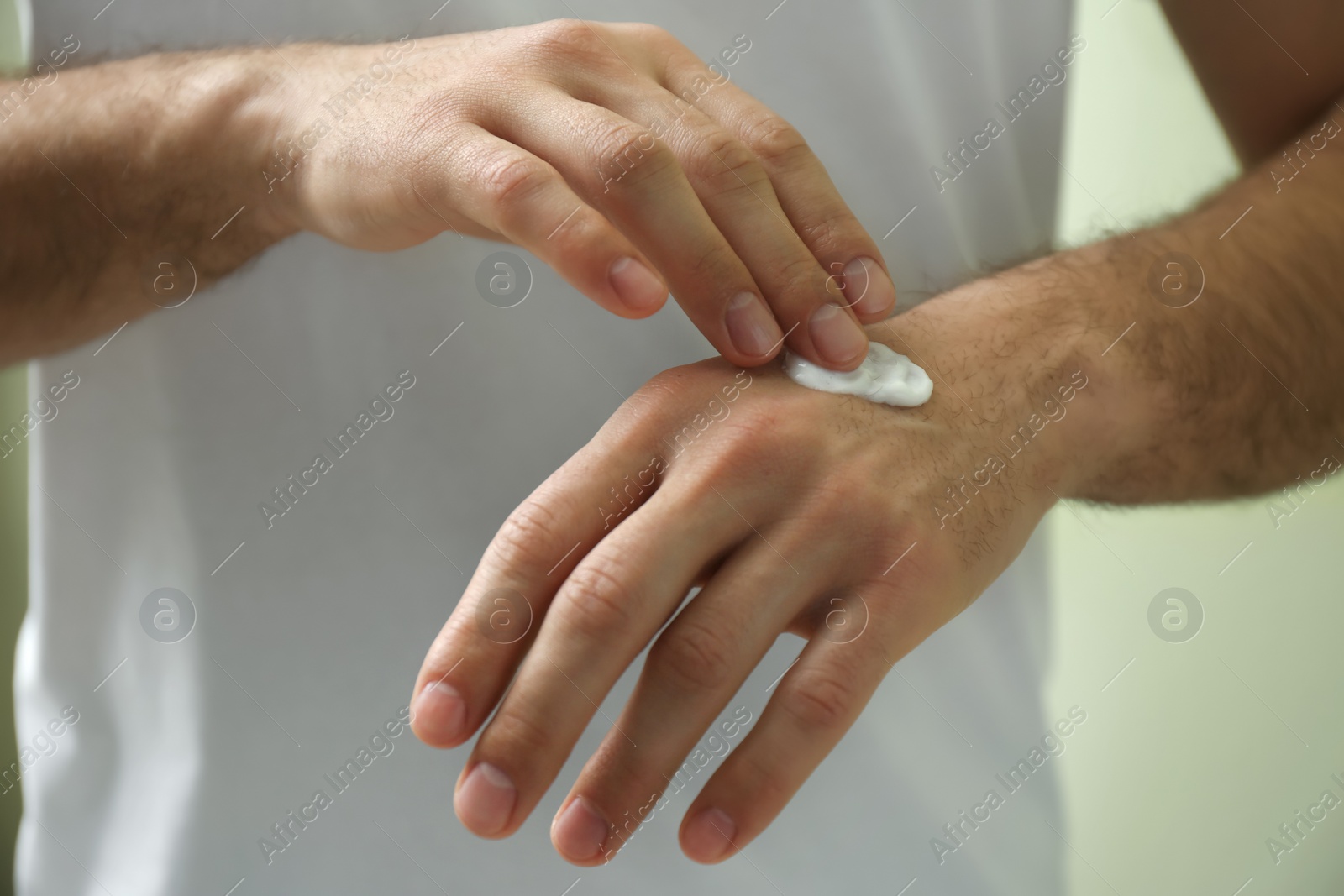 Photo of Man applying cream onto hand on green background, closeup