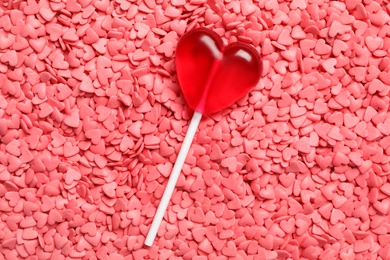 Sweet heart shaped lollipop on pink sprinkles as background, top view. Valentine's day celebration