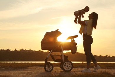 Happy mother with baby near river at sunset