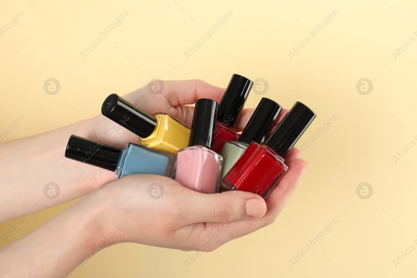 Photo of Woman holding nail polishes on beige background, closeup