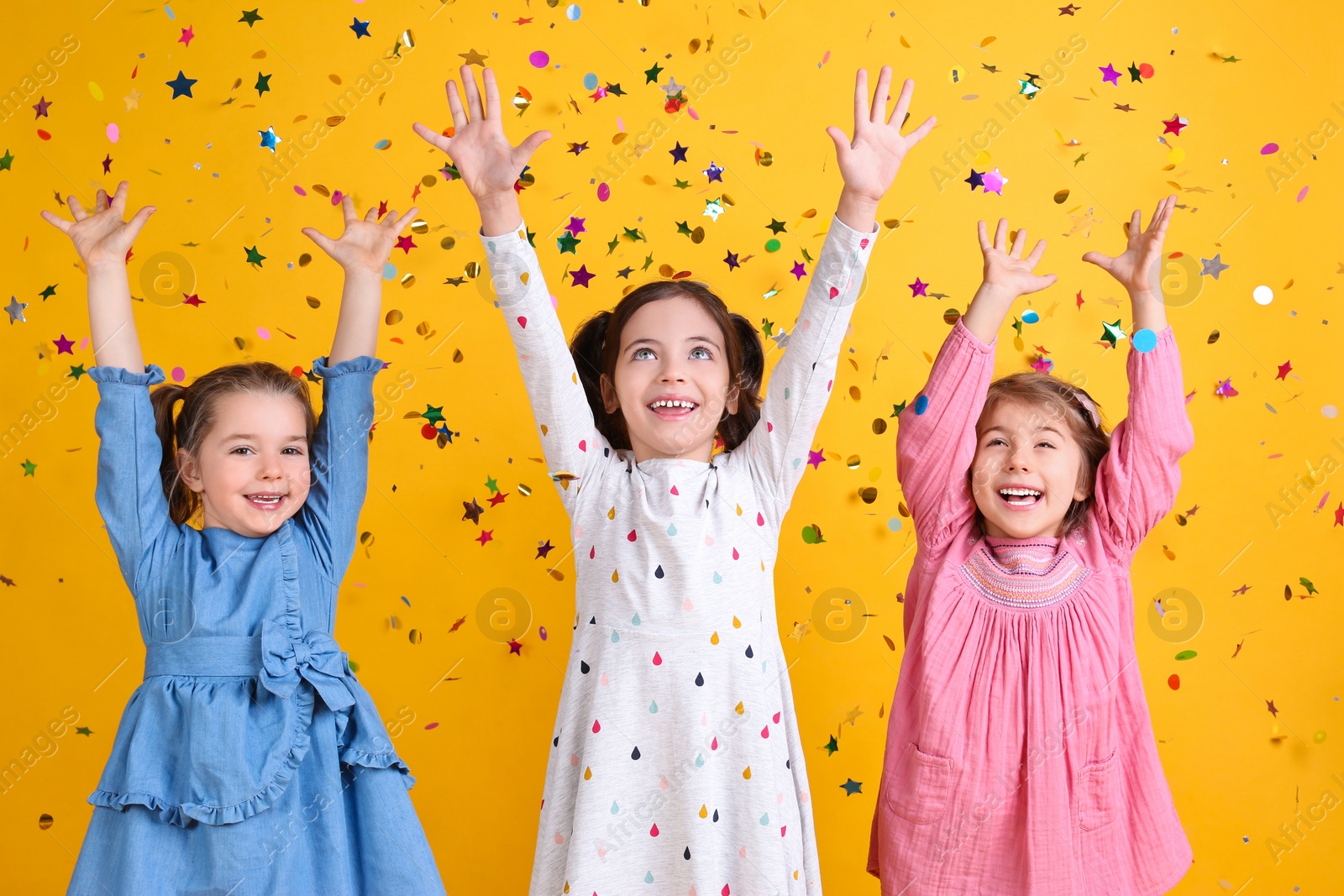 Photo of Adorable little children and falling confetti on yellow background