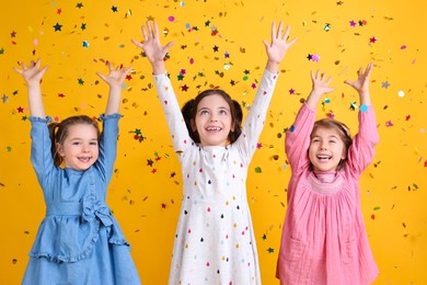 Photo of Adorable little children and falling confetti on yellow background