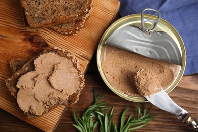 Open tin can with meat pate, fresh bread, knife and rosemary on wooden table, flat lay
