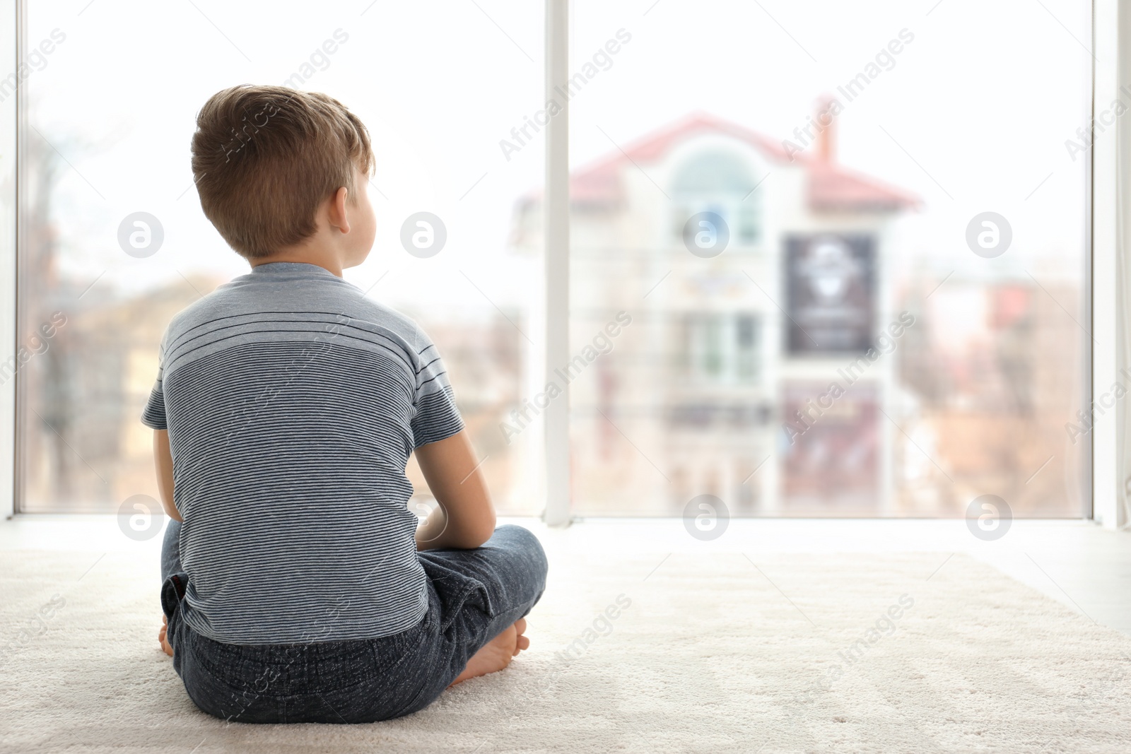 Photo of Lonely little boy sitting on floor in room. Autism concept