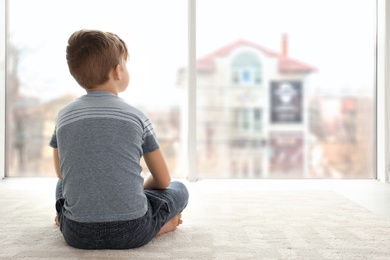 Photo of Lonely little boy sitting on floor in room. Autism concept