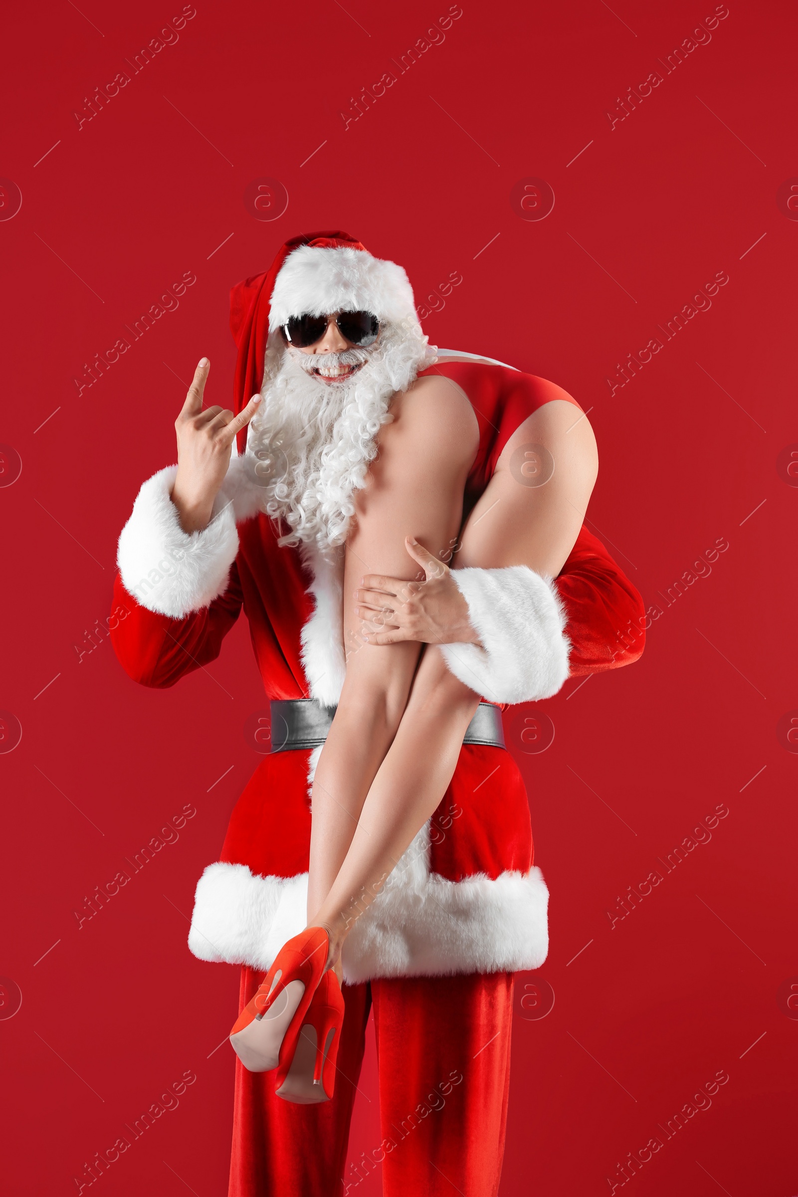 Photo of Young Santa Claus holding sexy naked woman on color background