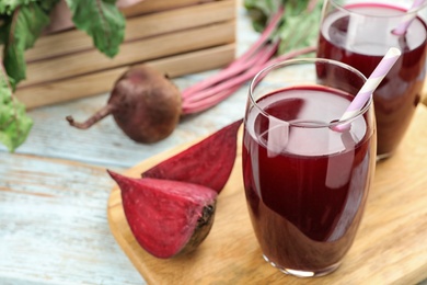 Wooden board with cut beet and glasses of juice on table. Space for text