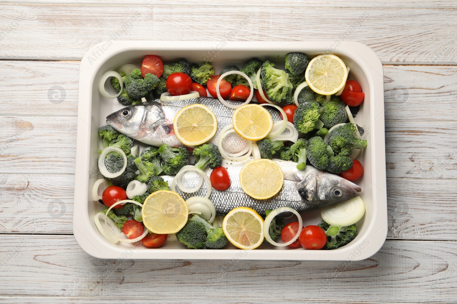 Photo of Raw fish with vegetables and lemon in baking dish on wooden table, top view