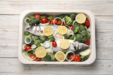 Raw fish with vegetables and lemon in baking dish on wooden table, top view