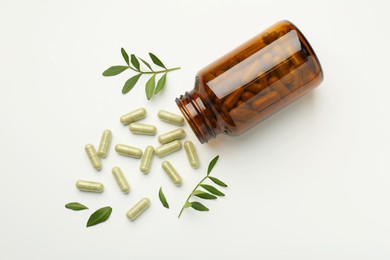 Bottle, vitamin capsules and leaves on white background, flat lay