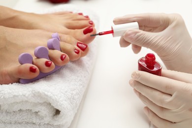 Photo of Pedicurist painting client`s toenails with red polish in beauty salon, closeup