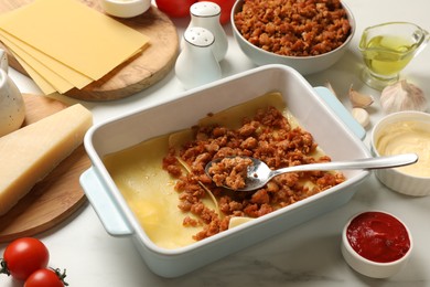 Photo of Cooking lasagna. Pasta sheets, minced meat and products in baking tray on white marble table