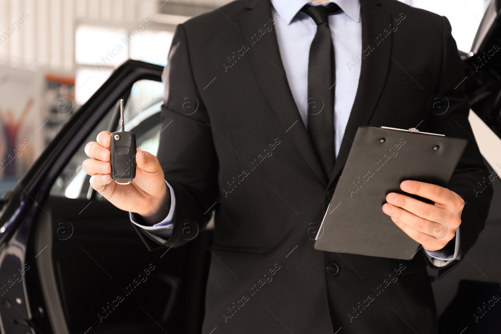 Photo of Salesman with key and clipboard near car in dealership, closeup