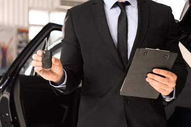 Salesman with key and clipboard near car in dealership, closeup