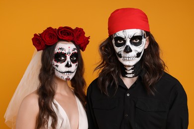 Couple in scary bride and pirate costumes on orange background. Halloween celebration
