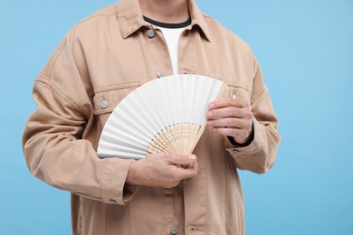 Photo of Man holding hand fan on light blue background, closeup