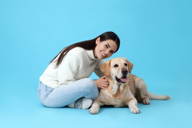 Happy woman with cute Labrador Retriever on light blue background