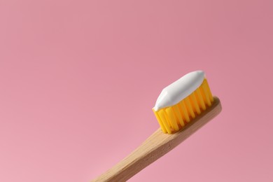 Photo of Wooden brush with toothpaste on pink background, closeup. Space for text