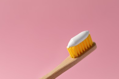 Wooden brush with toothpaste on pink background, closeup. Space for text