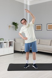 Photo of Senior man in sportswear stretching at home