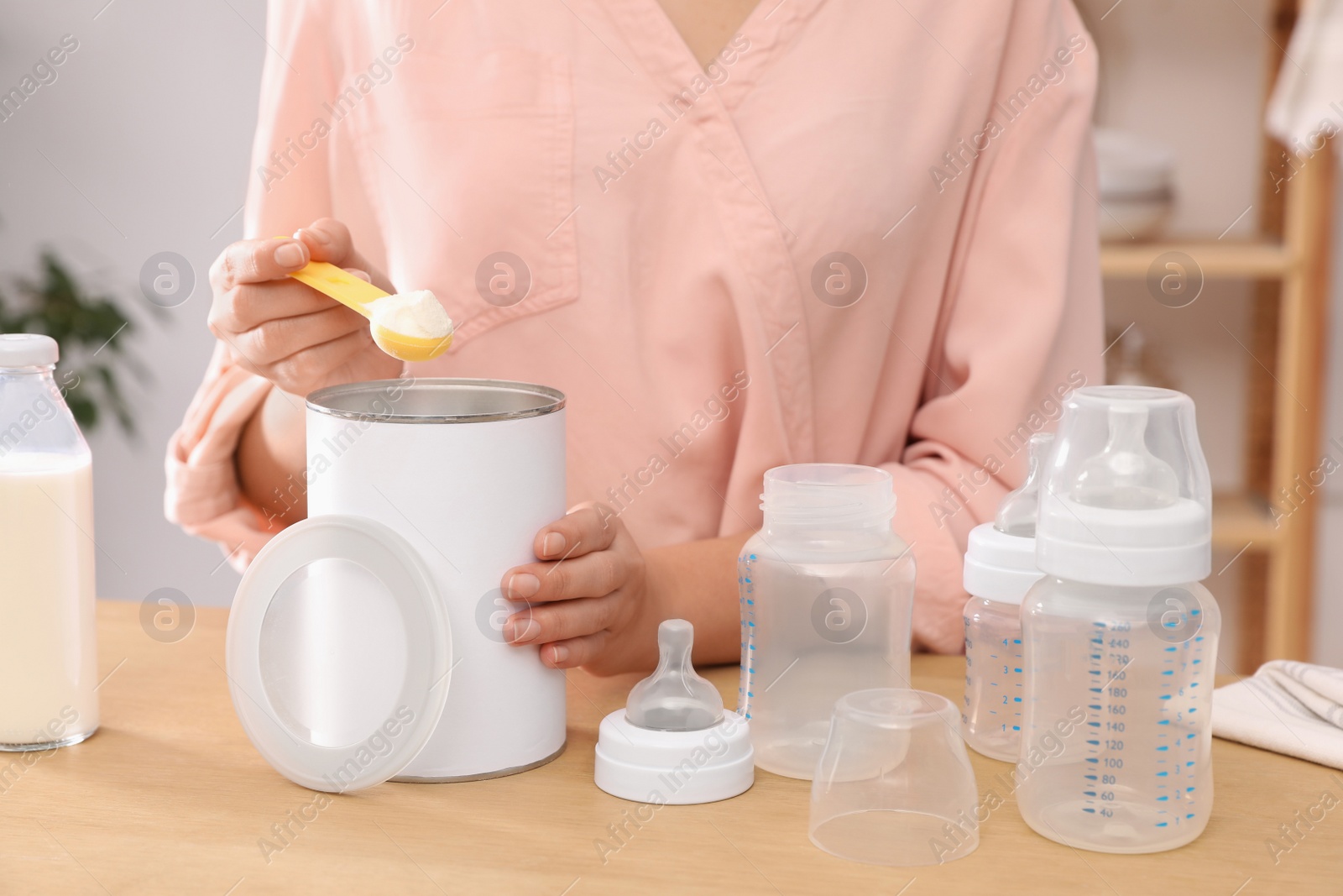 Photo of Woman preparing infant formula at table indoors, closeup. Baby milk